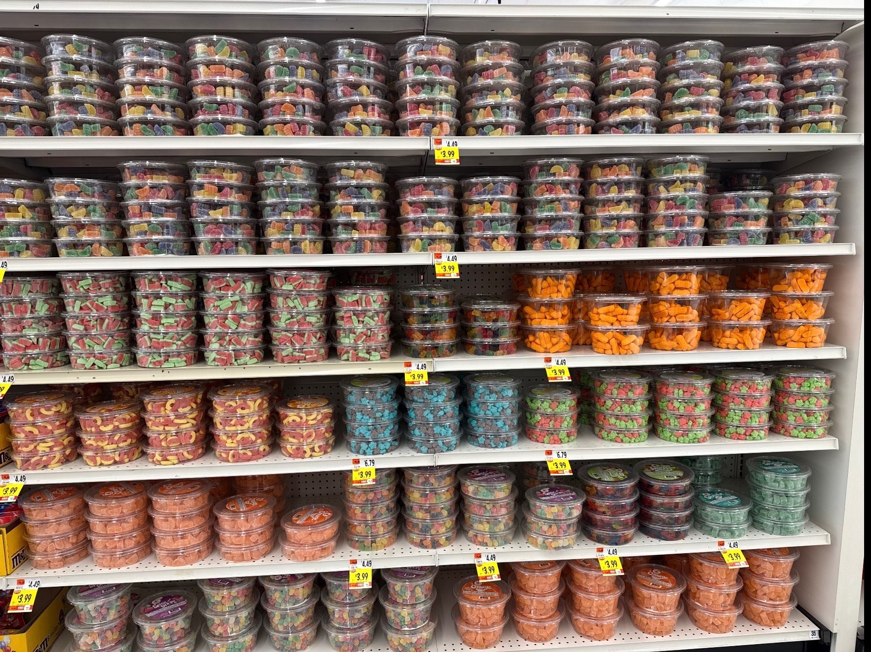Retail shelf stocked with clear plastic tubs of colorful candy in multiple flavors and sizes